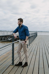 Young man standing on pier against sky