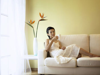 Portrait of woman having coffee while sitting on sofa at home
