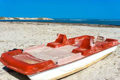 Red boat moored on beach against clear blue sky