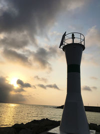 Silhouette lighthouse by sea against sky during sunset