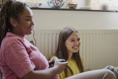 Smiling female teenager playing video game by friend at home