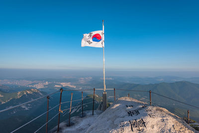 Flag on snow covered mountain against clear blue sky