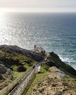 Low section of woman sitting on cliff by sea against clear sky