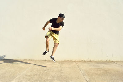 Full length of young man jumping on footpath against wall