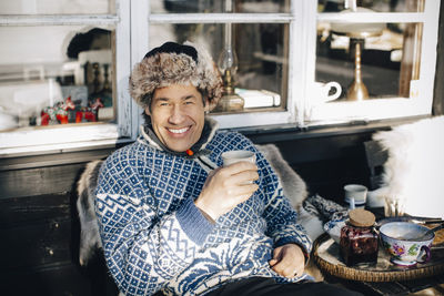 Portrait of happy mature man having coffee while sitting at porch during winter