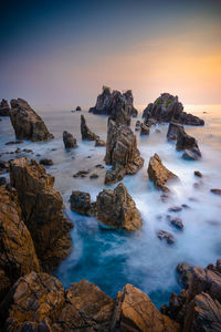 Rocks on beach against sky during sunset