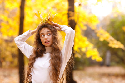 Portrait of young woman standing against trees during autumn