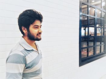 Side view of young man looking away while standing by wall