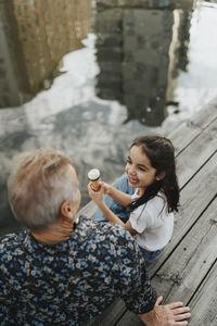 High angle view of girl with ice cream cone while looking at grandfather on jetty