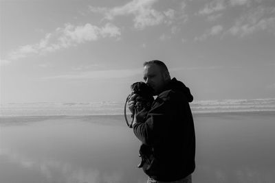 Portrait of man standing at beach with dog against sky