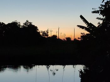 Silhouette trees by lake against sky during sunset