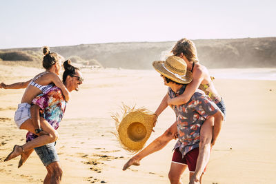 Men piggybacking girlfriends at beach against clear sky