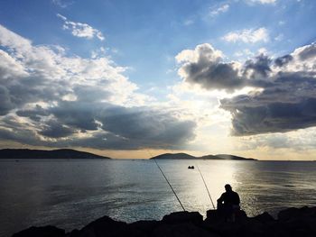 Silhouette man fishing at beach against sky