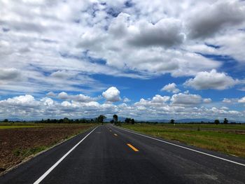 Empty road amidst field against sky