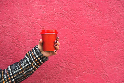 Close-up of hand holding disposable coffee cup against red wall