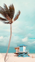 Tree and lifeguard hut at beach against sky