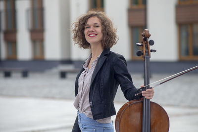 Portrait of smiling woman holding violin on street