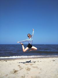 Portrait of teenage girl jumping at beach against clear blue sky