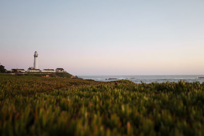 Lighthouse by sea against sky during sunset