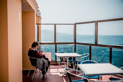 Woman sitting on terrace by sea against sky