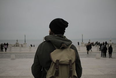 Rear view of man wearing backpack while standing at beach against clear sky