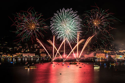 Firework display by lake in city at night