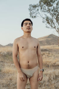 Portrait of shirtless man standing on field against sky