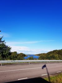 Road by trees against blue sky