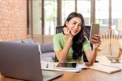 Young woman using phone while sitting on table