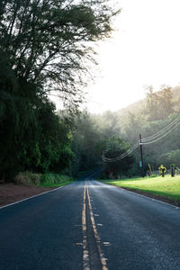 Empty road amidst trees against sky during sunrise