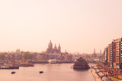 Boats in river by buildings in city against sky