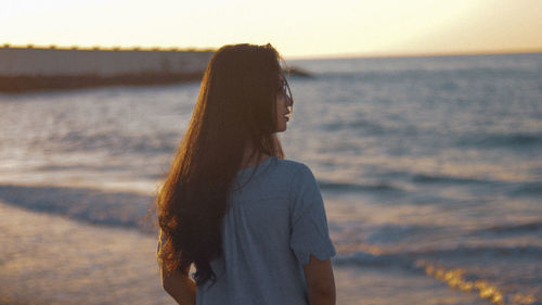 Woman standing at beach against sky during sunset