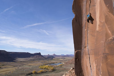 Low angle view of man rock climbing against blue sky