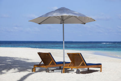 Deck chairs on beach against sky