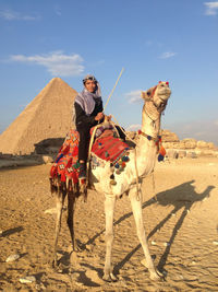 Man riding camel on sand against sky, giza pyramid of egypt