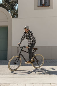 Confident man riding bicycle on street against building during sunny day