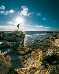 Man standing on rock by sea against sky