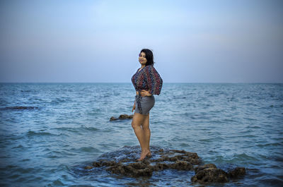 Full length of young woman standing on rock against sea