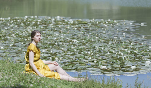 Side view of young woman sitting by lake