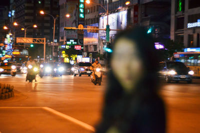 Woman against illuminated vehicles on city street at night