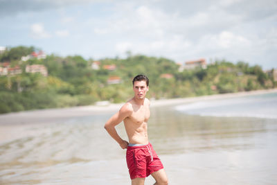 Shirtless young man looking away while standing at shore