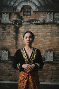 Portrait of woman standing against brick wall