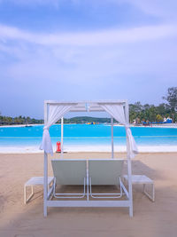 Chairs on beach by swimming pool against sky
