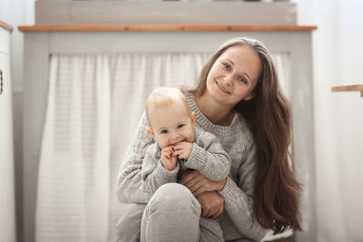 Happy mother and baby hugging, closeup portrait in bright room. beautiful mom with long wavy hair