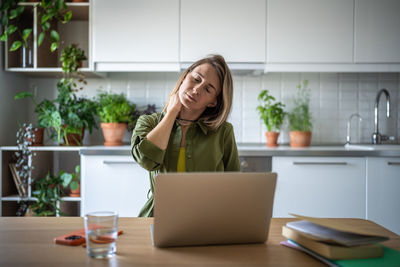 Freelance female working at home, sitting in curved position for long time, having pain in neck