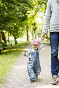 Portrait of baby girl holding mother's hand while walking on footpath