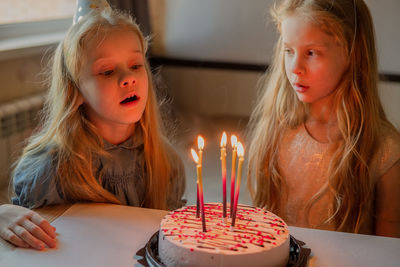 Little twin girls, children blow out candles cake birthday party at home. holiday during quarantine