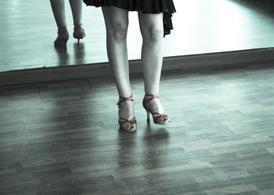 Low section of woman in high heels standing on hardwood floor