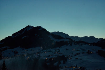 Aerial view of town by mountains against clear blue sky