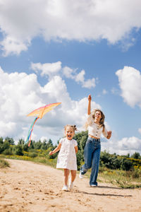 A laughing little girl and her mother run along the road to the field and fly a kite. 